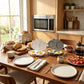 A breakfast table set in a warm kitchen, featuring two cat-shaped cookware pans in white and gray, filled with eggs, alongside plates, bread, coffee, and a toaster.