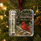 A clear acrylic Christmas ornament hanging on a Christmas tree, featuring a red cardinal, snowflakes, the text 'A Cardinal Christmas Blessing,' a rolled dollar bill in a tube, and a dark red hanging ribbon.
