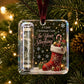 A clear acrylic Christmas ornament hanging on a decorated tree. The ornament contains a rolled dollar bill in one side and features festive graphics including a red stocking, candy cane, gifts, snowflakes, and the text 'A Little Christmas Cash In Your Stocking'.
