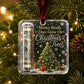 A clear acrylic Christmas ornament hanging from a green pine tree with warm string lights. The ornament contains a rolled dollar bill in a clear tube on the left and a printed Christmas tree scene with the phrase 'Money Really Does Grow On Christmas Trees' on the right.