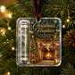 A square Christmas ornament hanging from a tree branch, featuring a rolled dollar bill and a printed holiday scene with stockings, gifts, and a fireplace. The ornament has a clear plastic border and a dark red hanging ribbon.
