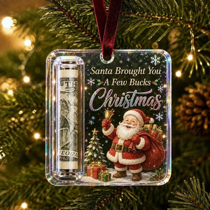 A square Christmas ornament hanging on a decorated tree. The ornament is clear and features a printed design with Santa Claus, a gift sack, a small tree, and the text 'Santa Brought You A Few Bucks Christmas.