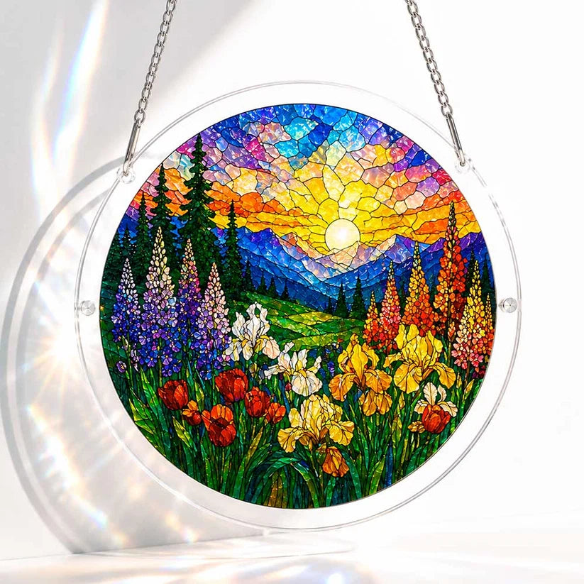 A round acrylic suncatcher showing a stained glass sunlit wildflower valley with iris tulips pine trees and distant mountains