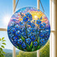 A round acrylic suncatcher with blue forget me not flowers and a glowing sun hanging from a chain in front of a bright white window