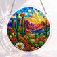 A round acrylic suncatcher depicting a desert sunset with saguaro cacti blooming cactus flowers and rocky mountains