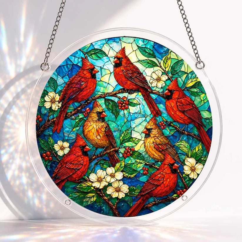 A round acrylic suncatcher with red and yellow cardinal birds perched among white blossoms berries and green leaves