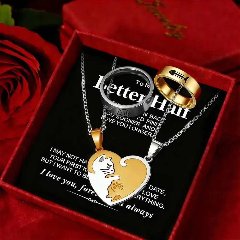 A jewelry gift set displayed inside a red presentation box with a red rose. The set includes a silver and gold heart pendant necklace with a cat design, a silver ring, and a gold fishbone ring, all on a black message card with romantic text.