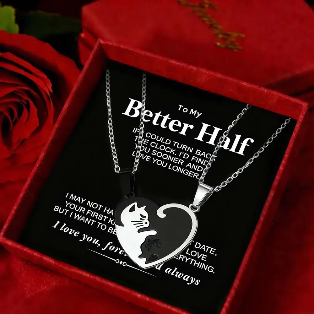 A silver heart-shaped pendant necklace with a cat silhouette cutout, displayed inside a red gift box with a black message card. Red roses are visible in the background.