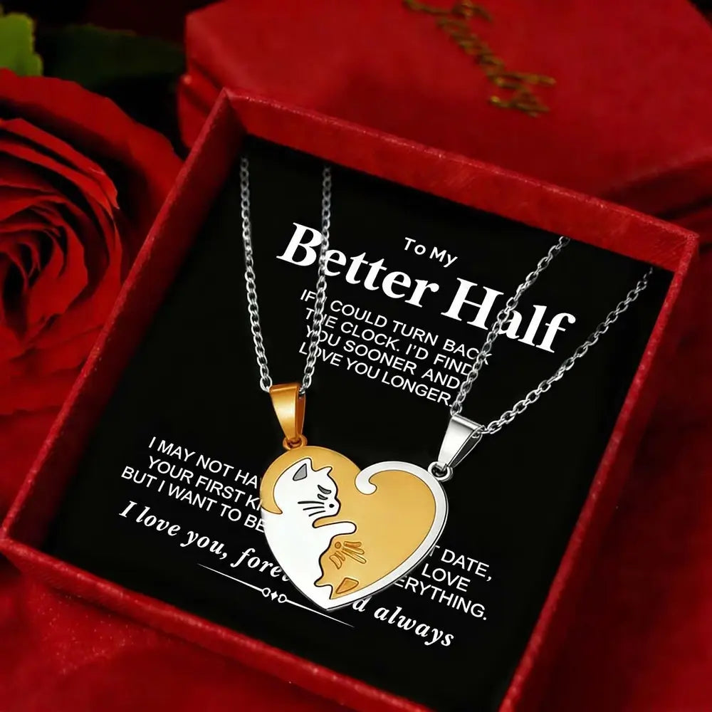 Two heart-shaped pendant necklaces displayed inside a red gift box with a black message card. One necklace is gold with a white cat silhouette, and the other is silver with a white cat silhouette.