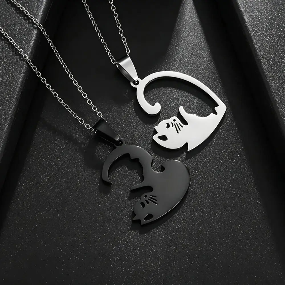 Two interlocking cat-shaped pendant necklaces on chains, one polished silver and one matte black, displayed on a textured black background.