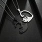 Two interlocking cat-shaped pendant necklaces on chains, one polished silver and one matte black, displayed on a textured black background.