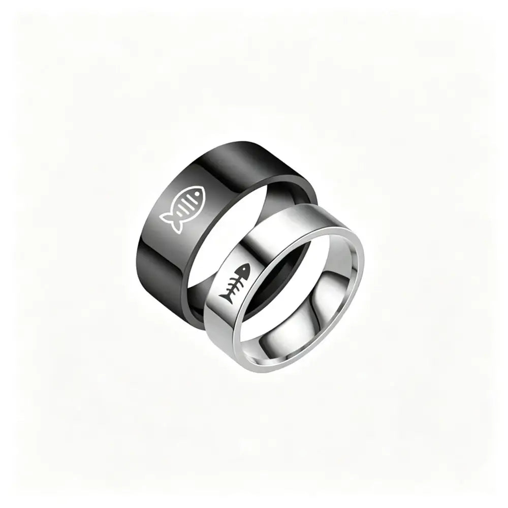 Two interlocking stainless steel rings on a plain white background. The top ring is black with a white fish symbol, and the bottom ring is silver with a black fish skeleton symbol.