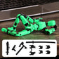 Green and black articulated robot toy figure posed on a wooden desk with a laptop blurred in the background, plus an inset showing included black accessories.