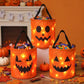 Three orange jack-o'-lantern-shaped fabric candy baskets with black handles and built-in warm white string lights, filled with assorted candies, displayed on a table in a Halloween-themed room with pumpkins and autumn leaves.