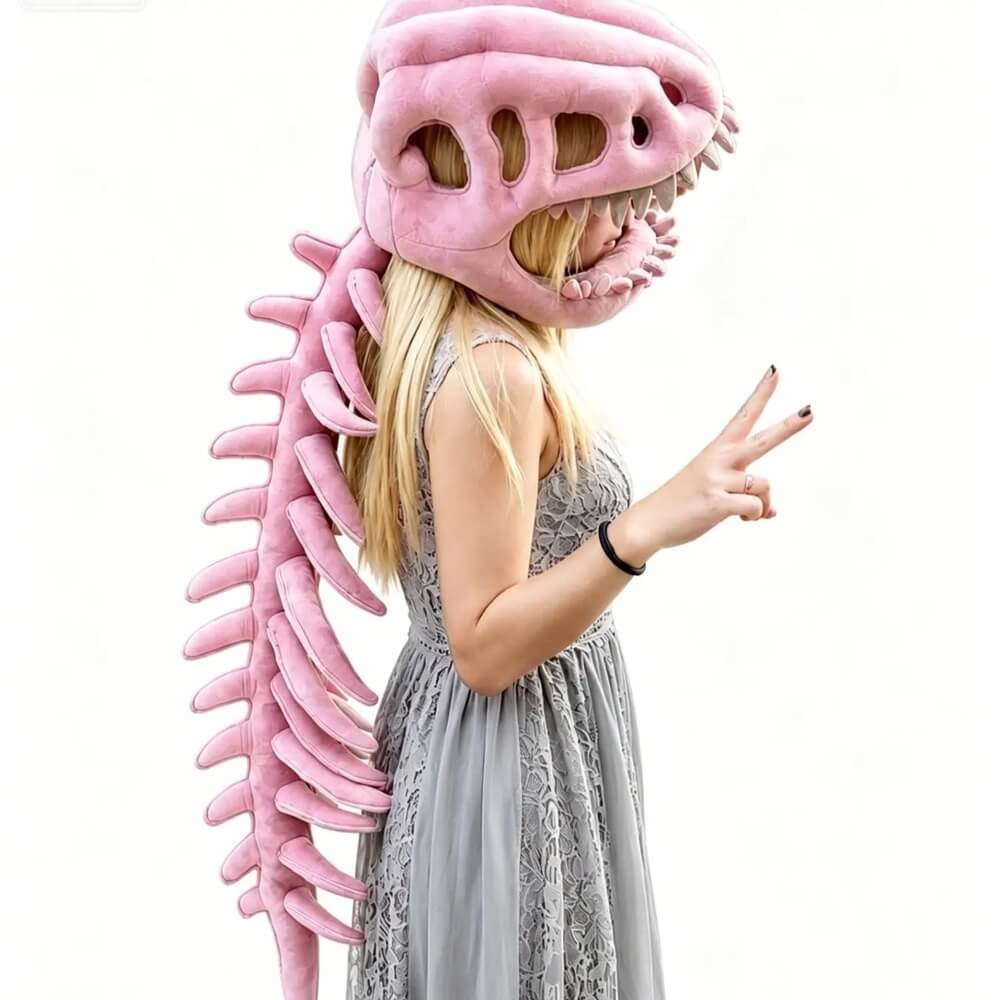 A woman wearing a pink dinosaur skull mask with sharp teeth and a long pink dinosaur spine costume accessory, posed against a plain white background.