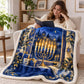 A woman in a beige sweater sits in an armchair reading with the blue Hanukkah menorah blanket draped over her lap beside a warm lit menorah