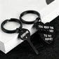 Two black metal keychains shaped like a broken heart and key, with white engraved text reading 'FOREVER' and 'YOU HOLD THE KEY TO MY HEART', displayed on stacked white books over a dark surface.