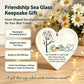 Heart-shaped sea glass keepsake ornament necklace with a printed design of two birds and a tree, shown hanging on a chain against a warm floral and string-light background. The image includes promotional text describing it as a friendship sea glass keepsake gift and listing features such as meaningful friendship symbol, elegant sea glass art decor, ready-to-go gift box, and perfect for birthdays, holidays, and thank-you moments.