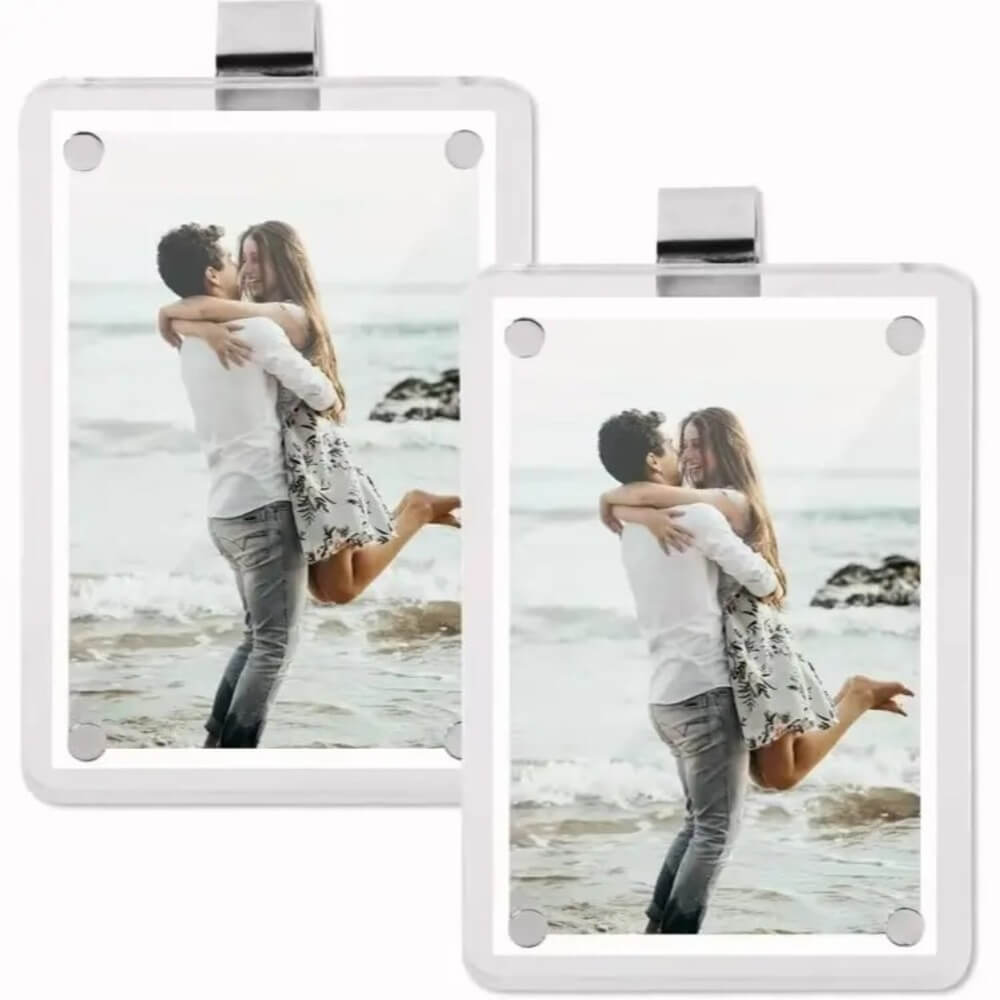 Two white square picture frames with rounded corners and a silver metal clip at the top, shown on a white background. Each frame contains a photo of a couple embracing on a beach.