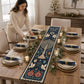 A woman in soft white outfit arranges tableware around the navy Hanukkah table runner for holiday dinner preparation