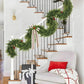 Decorative Christmas garland on a staircase with a white chair and gift bag in the foreground.