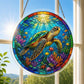 A round acrylic suncatcher with a sea turtle swimming among tropical fish coral and starfish hanging from a chain in front of a white window