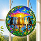 A round acrylic suncatcher with six cats sitting on a wooden fence watching a sunset hanging from a chain in front of a bright white window