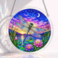 A round acrylic suncatcher with a blue dragonfly hovering over pink lotus flowers and a calm lake at twilight